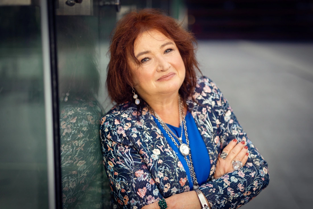 Portret kobiety w kwiecistej marynarce, uśmiechającej się i opierającej na szkle.