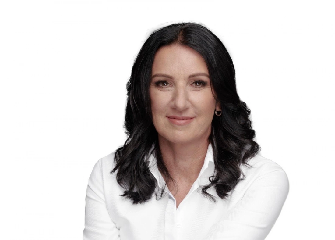 Kobieta o ciemnych, falowanych włosach uśmiechająca się, ubrana w białą koszulę.