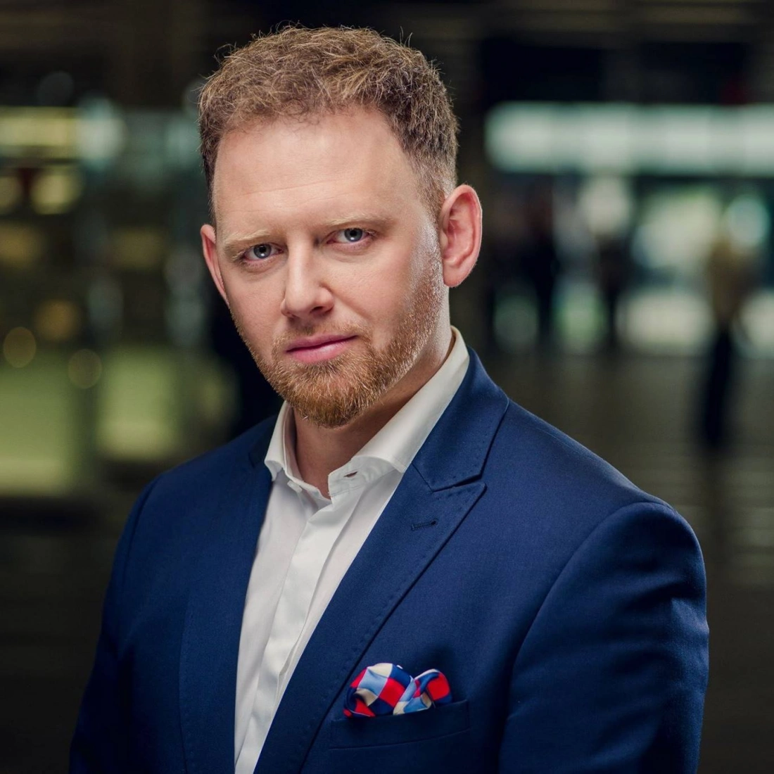 Mężczyzna w eleganckim, granatowym garniturze z białą koszulą i kolorową poszetką.