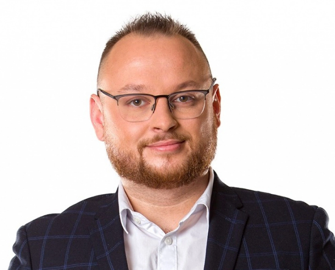 Mężczyzna w okularach, z zarostem, ubrany w marynarkę w kratę.