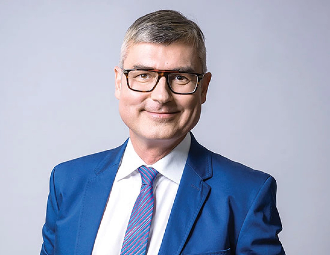 Mężczyzna w okularach, uśmiechający się, ubrany w niebieski garnitur.