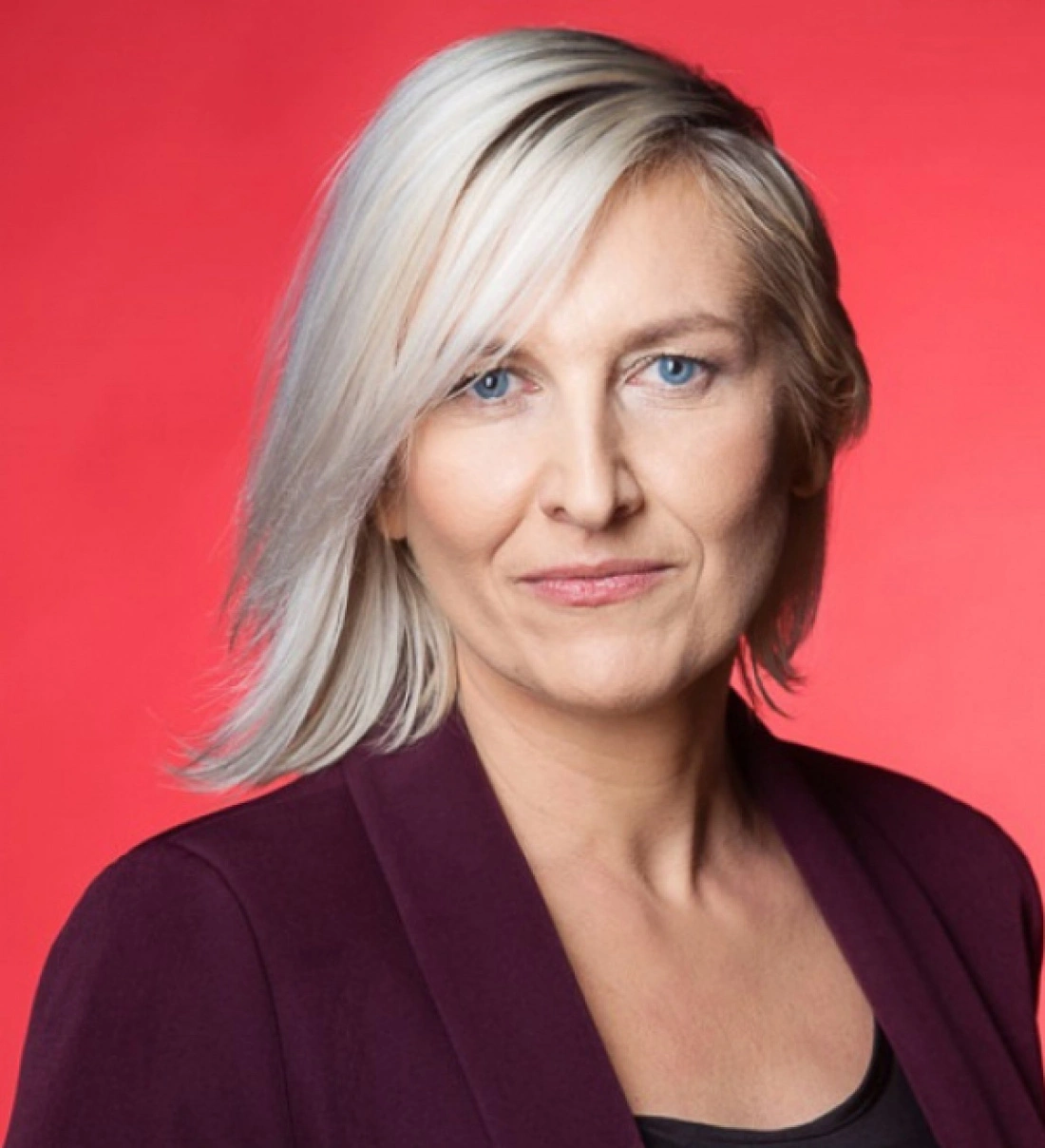Portret kobiety z jasnymi włosami na tle w kolorze czerwonym.