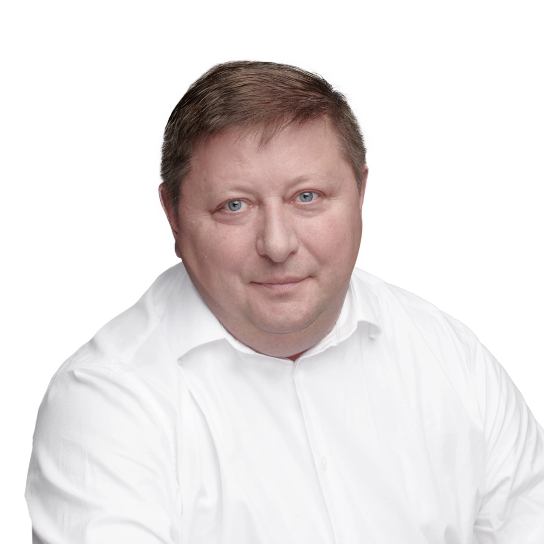 Mężczyzna w białej koszuli, patrzący w kamerę na jasnym tle.