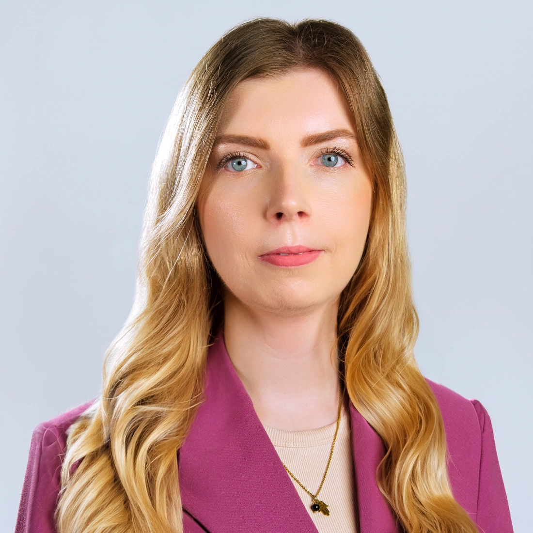 Portret kobiety z długimi, falującymi włosami, w różowym garniturze, na jednolitym tle.