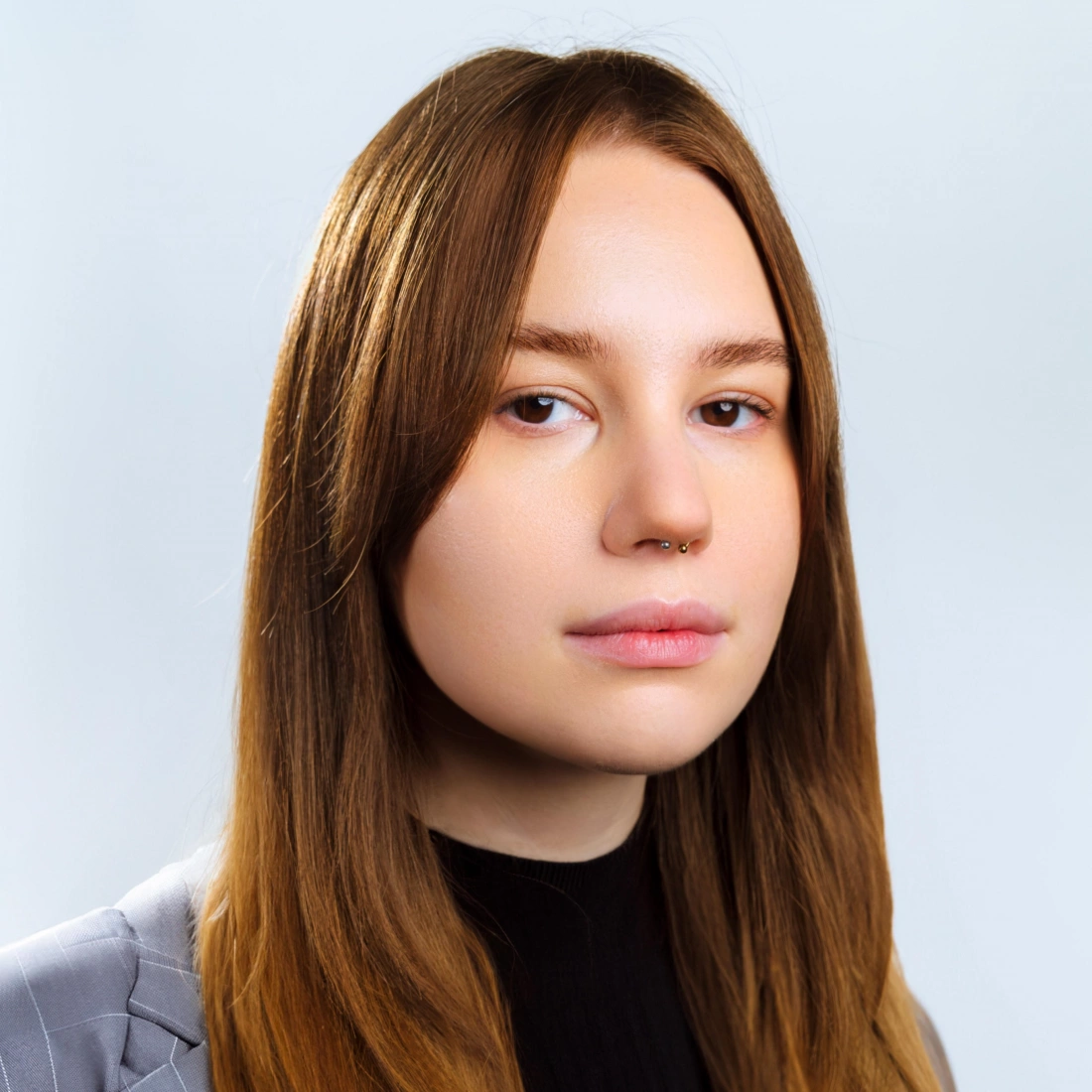 Portret młodej osoby z długimi, prostymi włosami i delikatnym piercingiem w nosie.