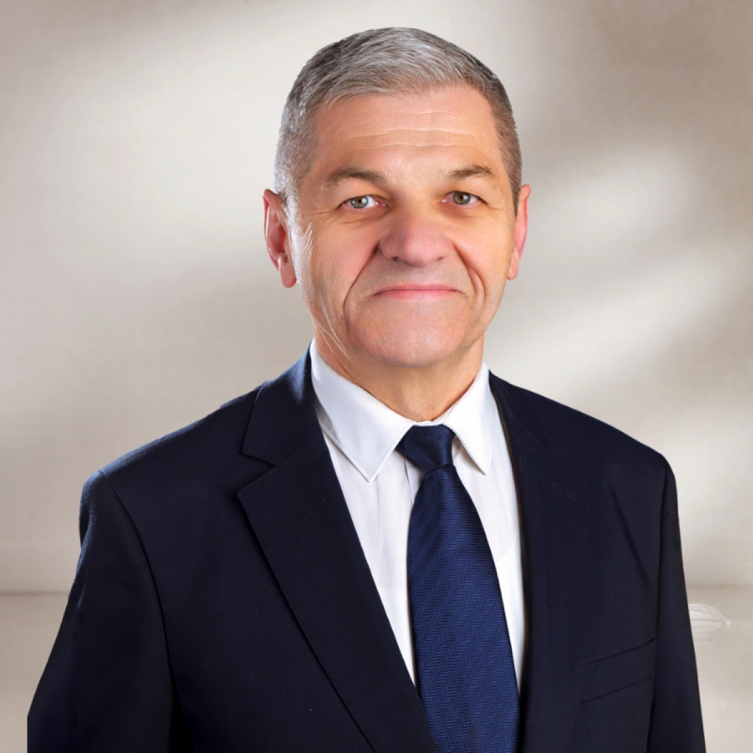 Mężczyzna w garniturze i krawacie, uśmiechający się na neutralnym tle.