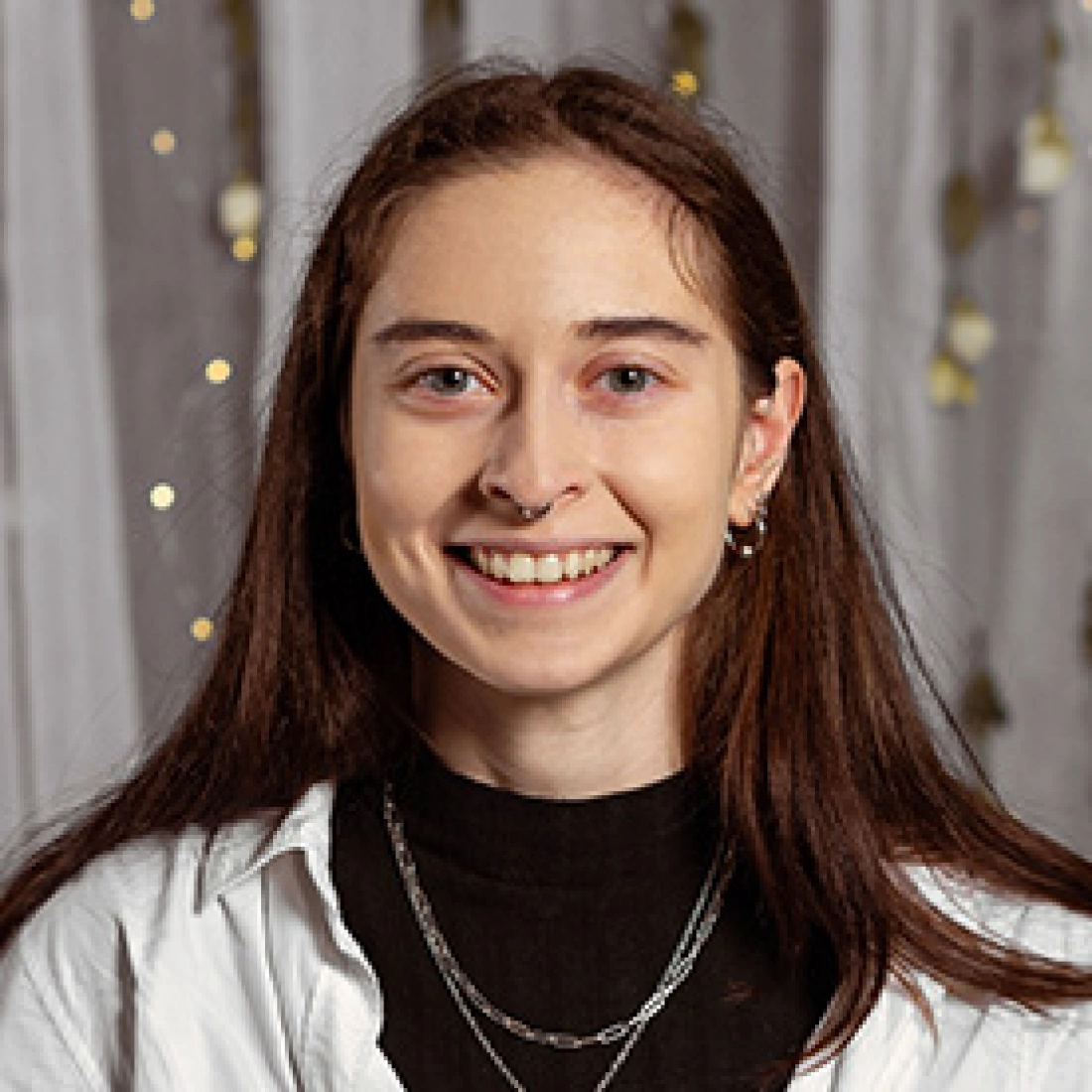 Młoda osoba z długimi włosami, uśmiechająca się w jasnym otoczeniu.