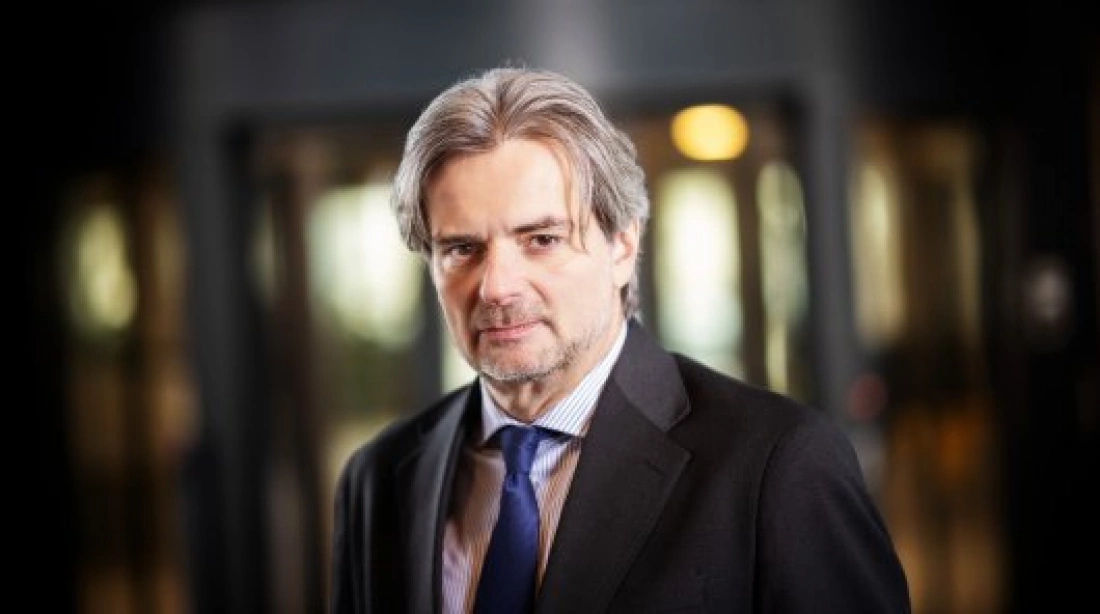 Mężczyzna w garniturze z siwymi włosami, stojący w eleganckim otoczeniu.