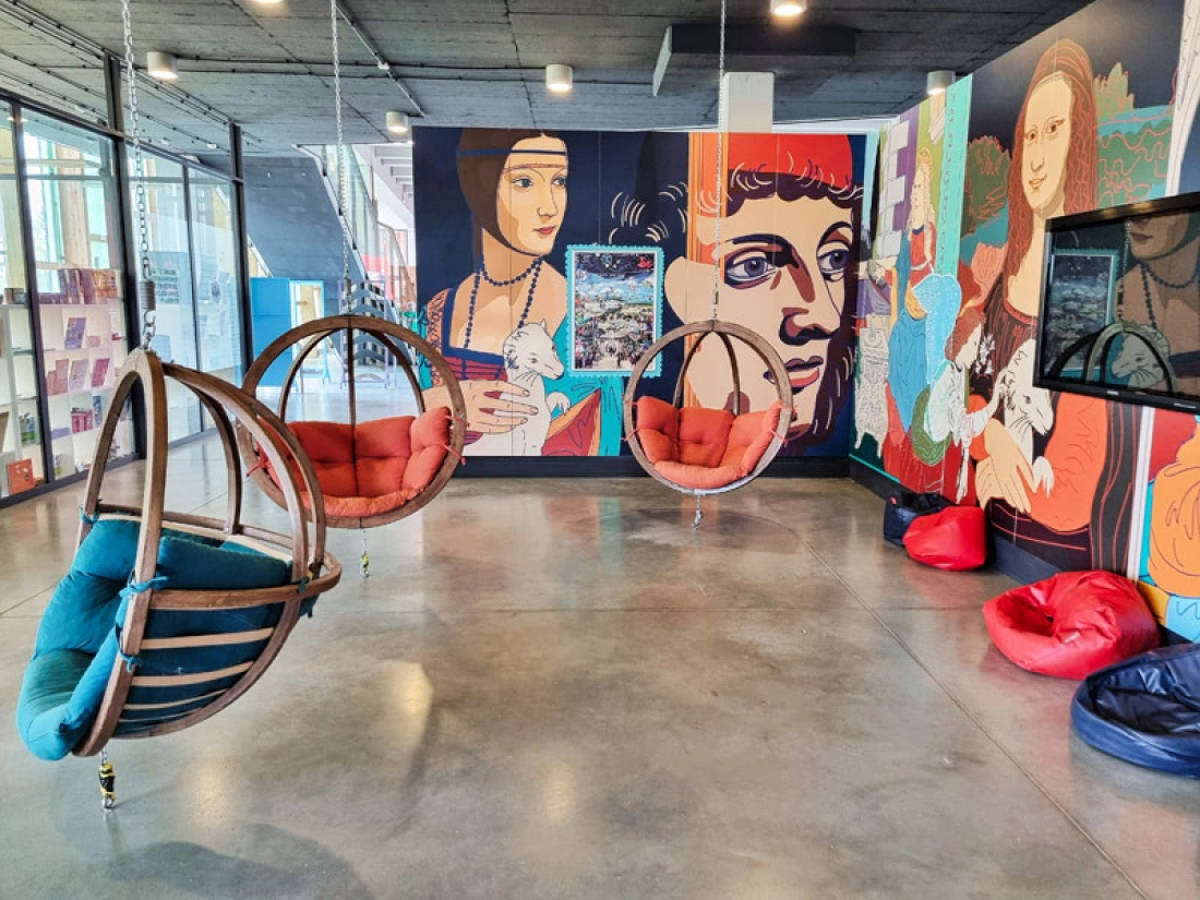 Nowoczesne wnętrze z wiszącymi fotelami i muralami przedstawiającymi znane obrazy.