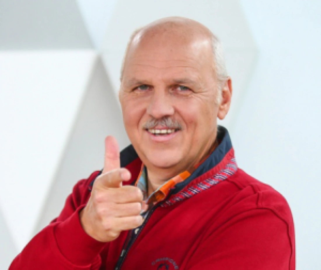 Mężczyzna w czerwonym swetrze uśmiecha się i pokazuje gest „ok”.