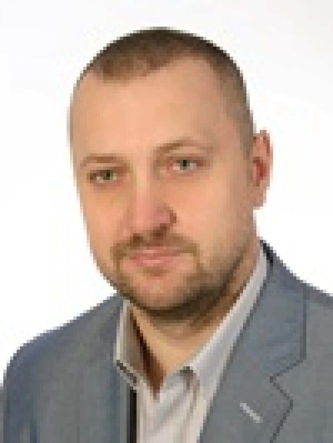 Mężczyzna w szarym garniturze, na jasnym tle, z poważnym wyrazem twarzy.