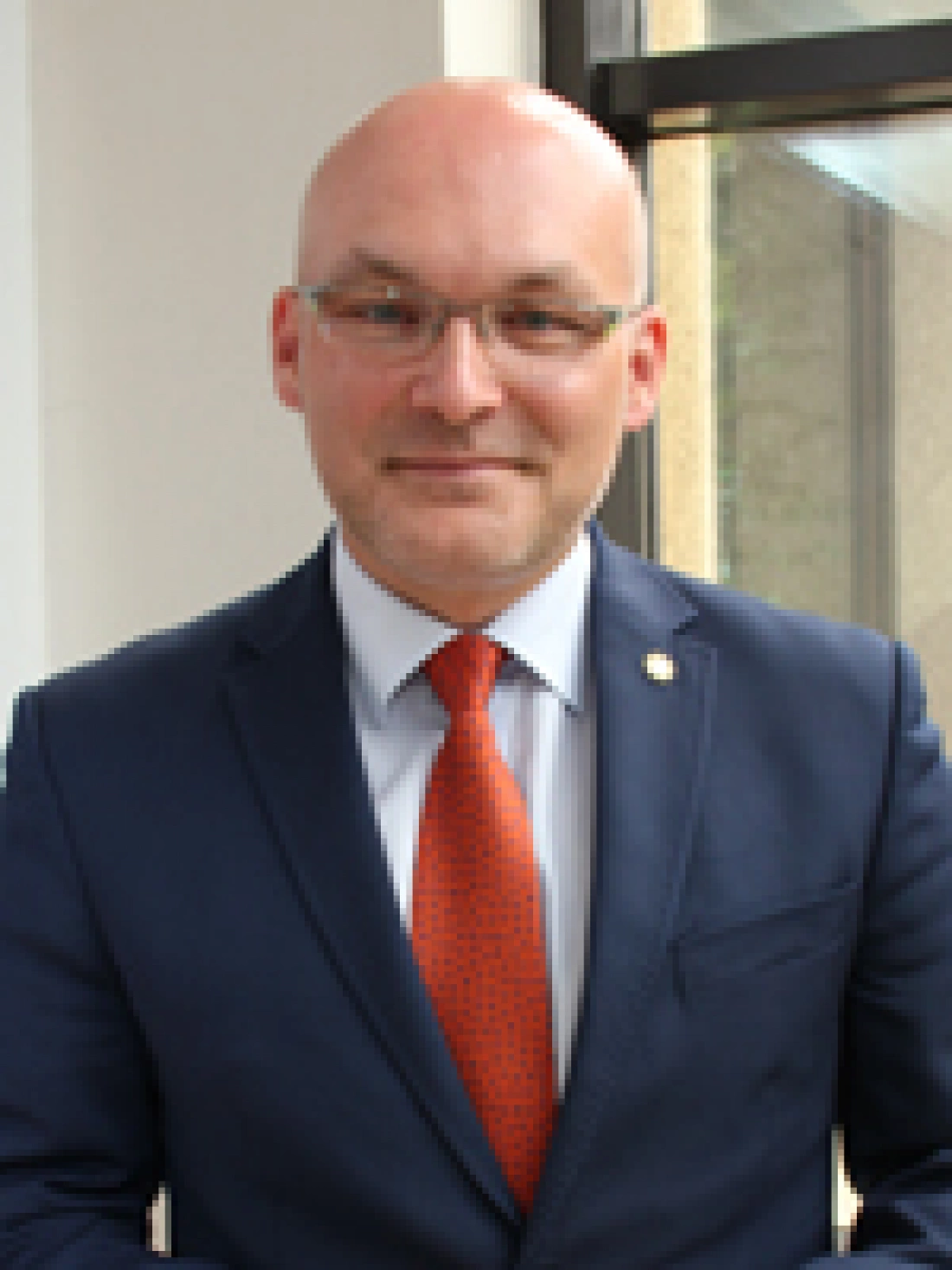 Mężczyzna w garniturze z pomarańczowym krawatem stoi przy oknie.