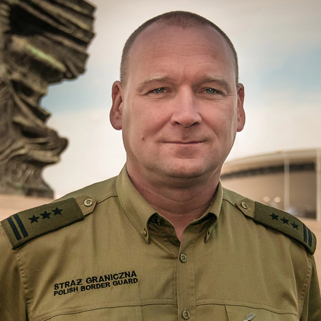 Portret mężczyzny w mundurze Straży Granicznej, z tłem architektonicznym.