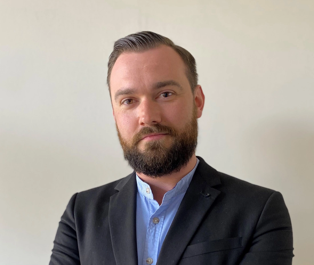 Mężczyzna w garniturze z brodą, z poważnym wyrazem twarzy.