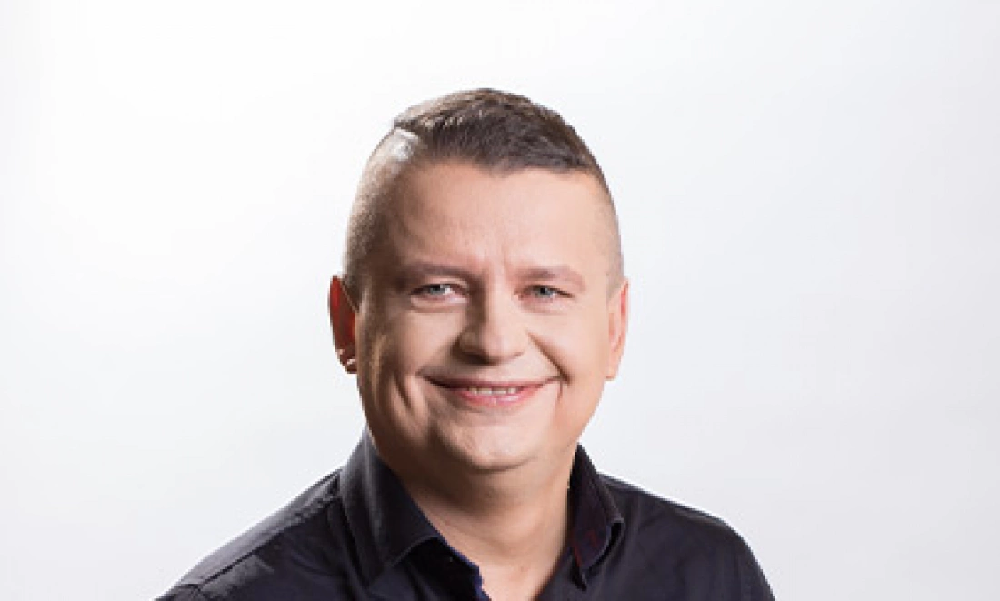 Uśmiechnięty mężczyzna w czarnej koszuli na jasnym tle.