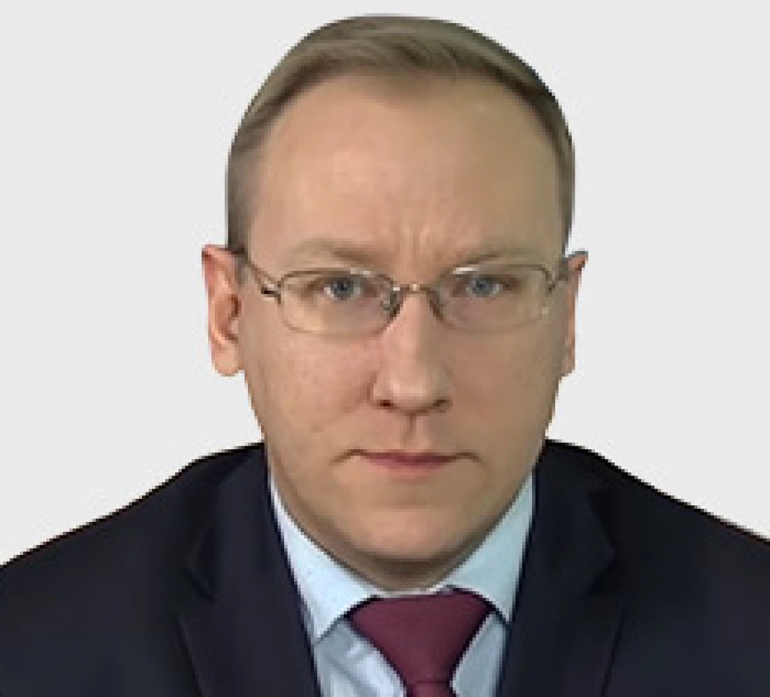 Mężczyzna w okularach, ubrany w garnitur, z poważnym wyrazem twarzy.