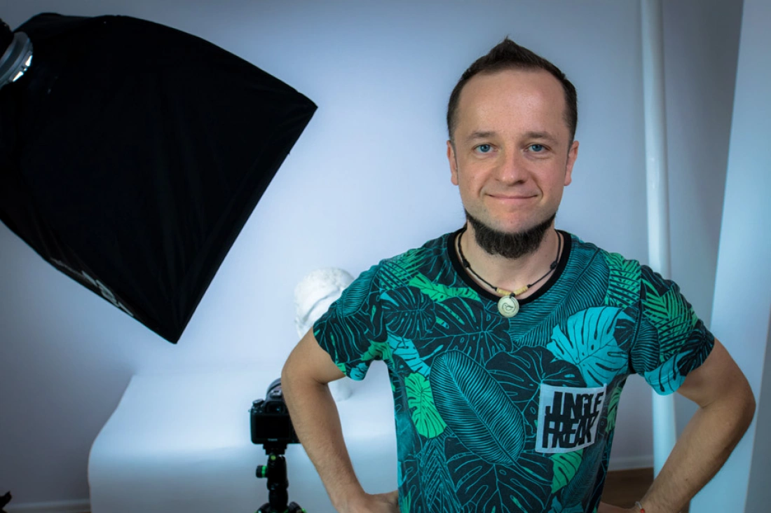 Mężczyzna z uśmiechem stoi w studio fotograficznym, z oświetleniem w tle.