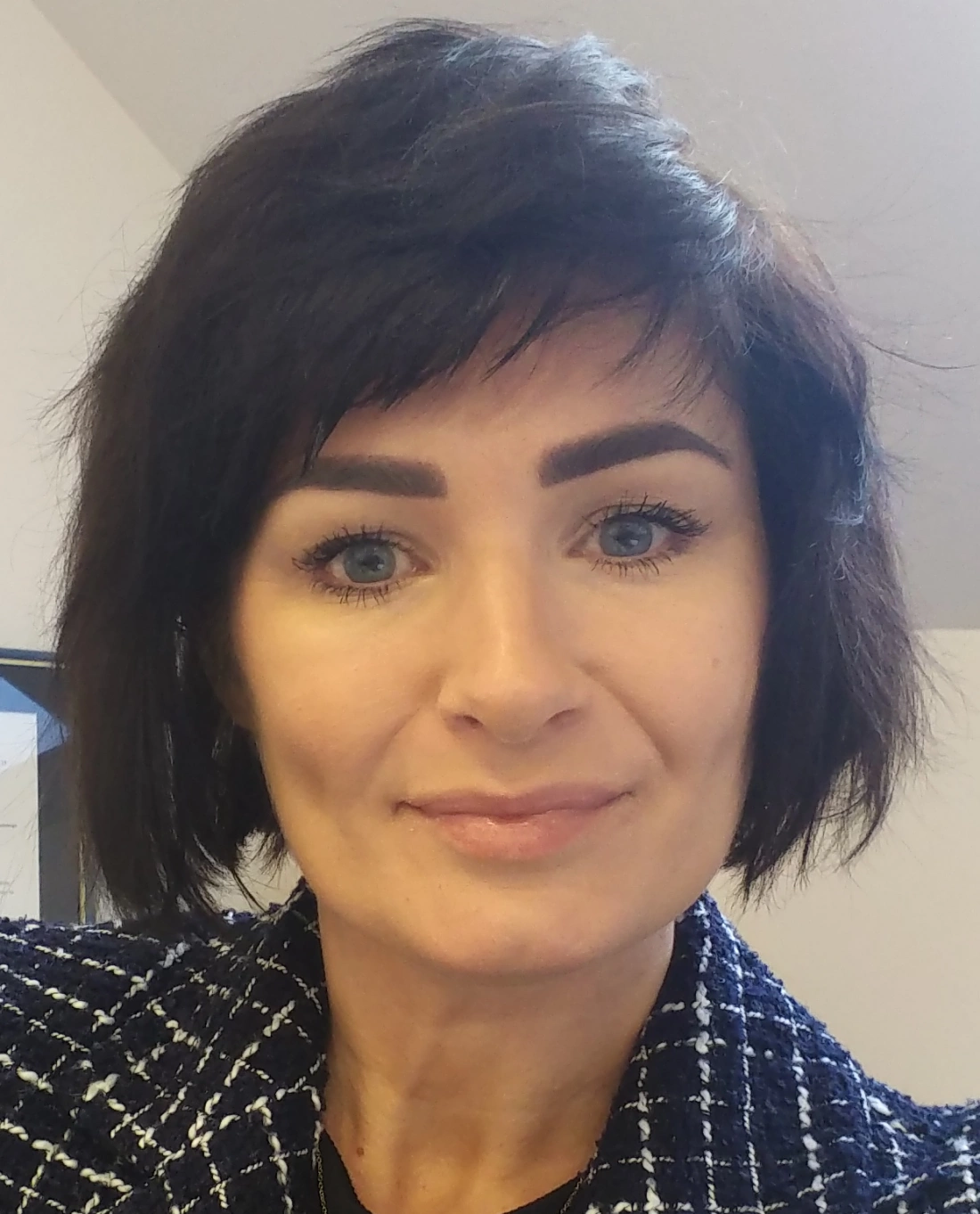 Portret kobiety z krótkimi, ciemnymi włosami i niebieskimi oczami, uśmiechającej się do aparatu.