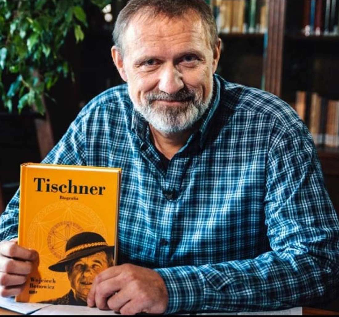 Mężczyzna w koszuli w kratę trzyma książkę o Tischnerze w bibliotece.