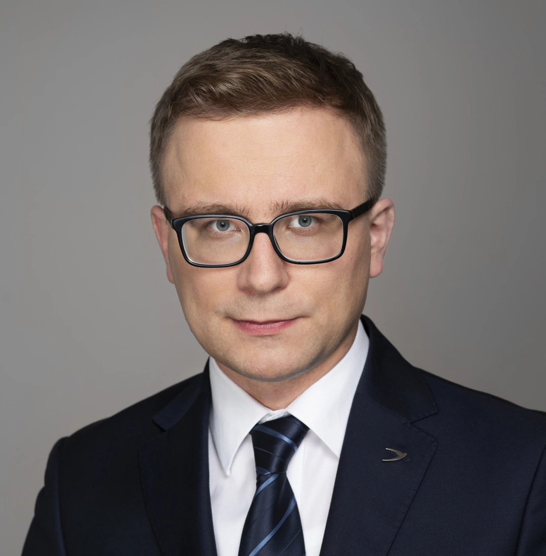 Mężczyzna w okularach, w garniturze, z poważnym wyrazem twarzy.