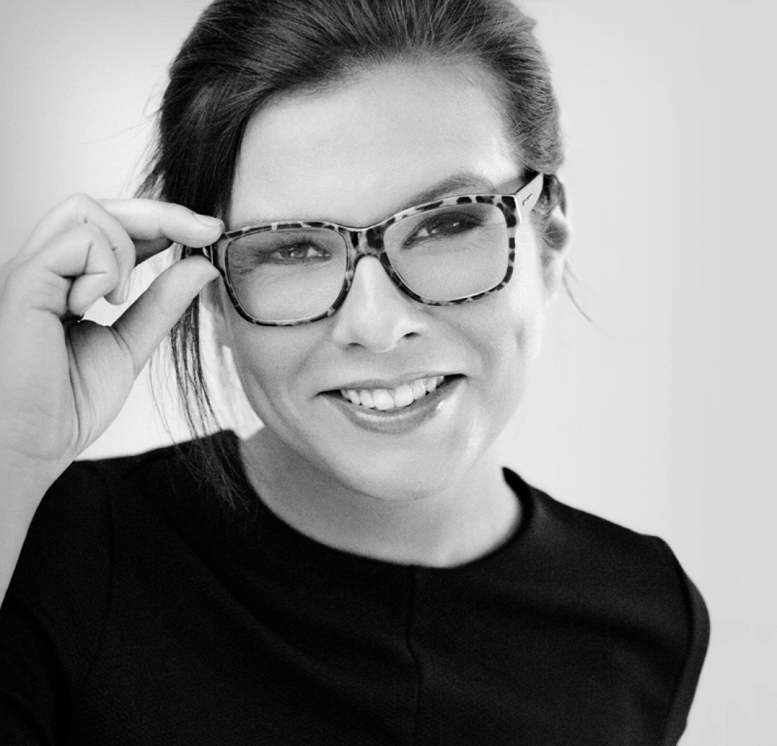 Kobieta w okularach, uśmiechająca się i podtrzymująca szkła.