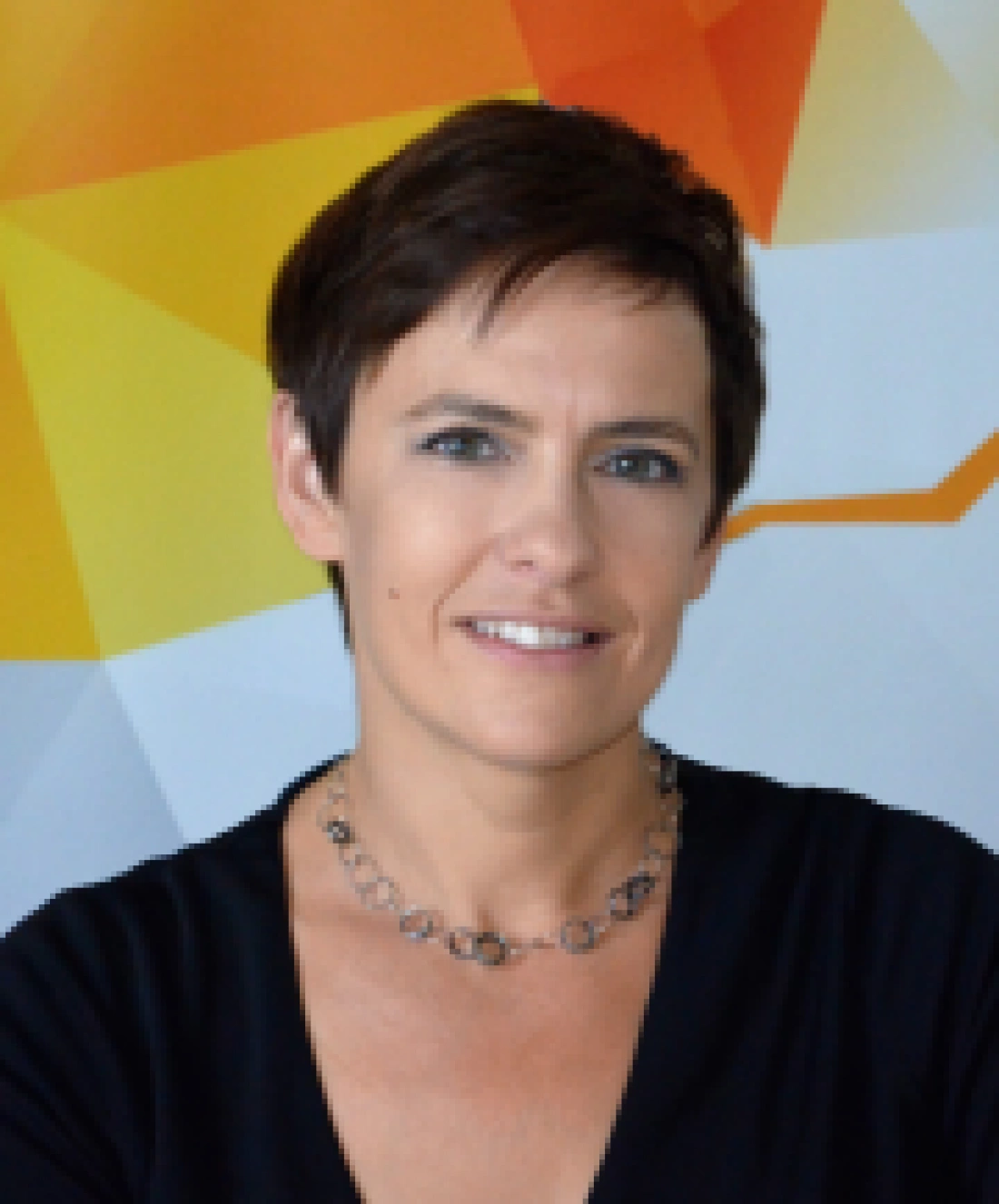Kobieta z krótkimi włosami, ubrana na czarno, uśmiecha się, stojąc przed kolorowym tłem.