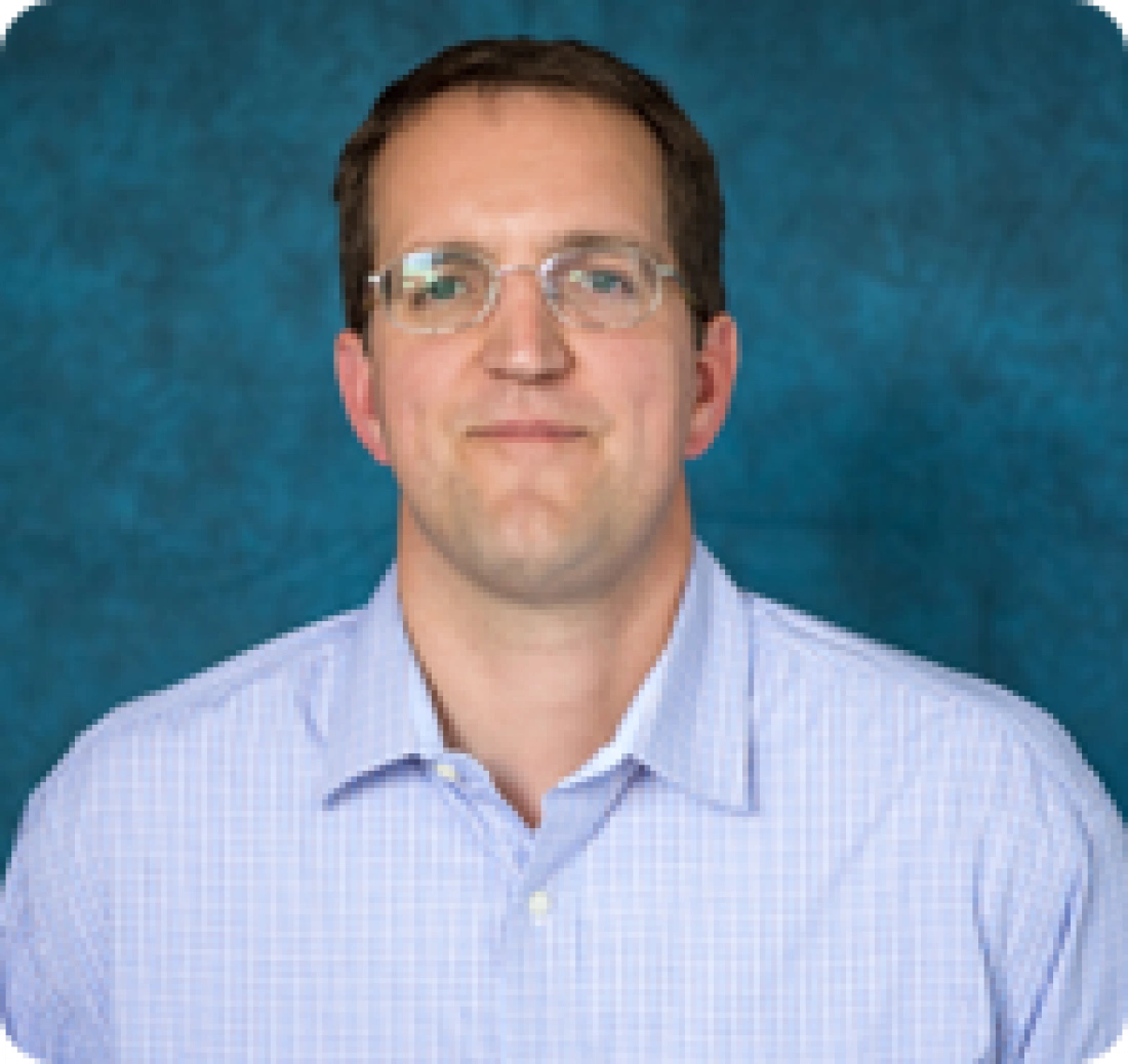 Mężczyzna w okularach, ubrany w niebieską koszulę, na tle w odcieniach niebieskiego.