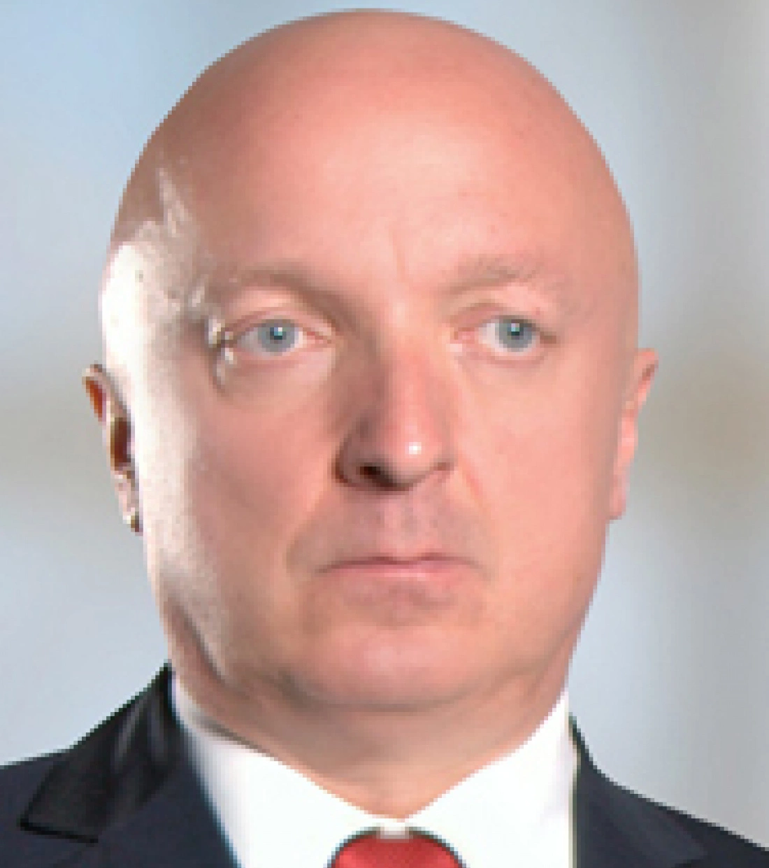 Mężczyzna z łysą głową, w garniturze i krawacie, patrzy w obiektyw.