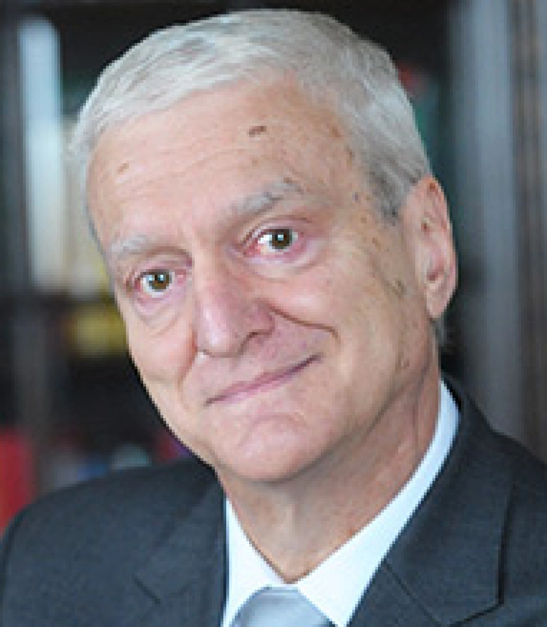 Mężczyzna w garniturze z siwymi włosami, uśmiechający się do kamery.