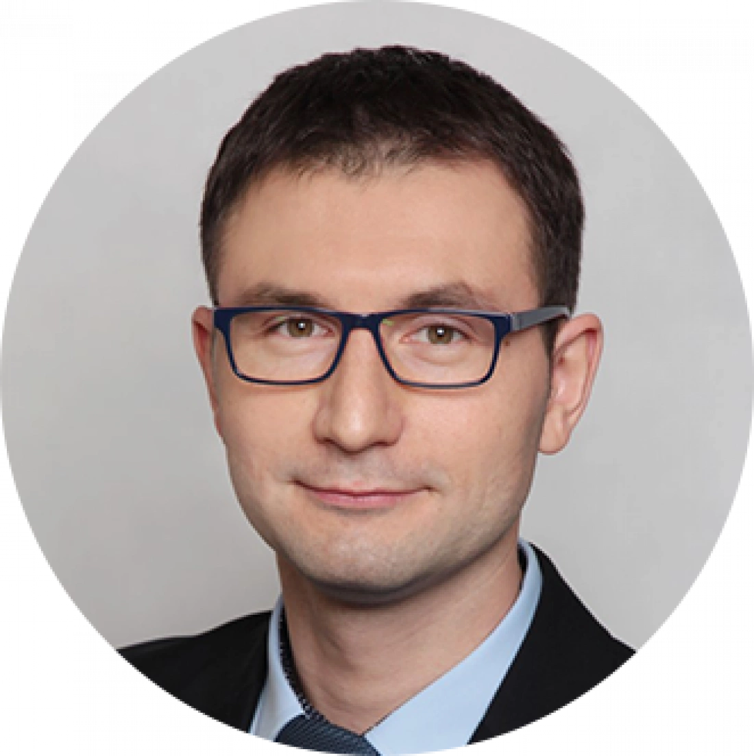Mężczyzna w okularach, ubrany w garnitur, na neutralnym tle.