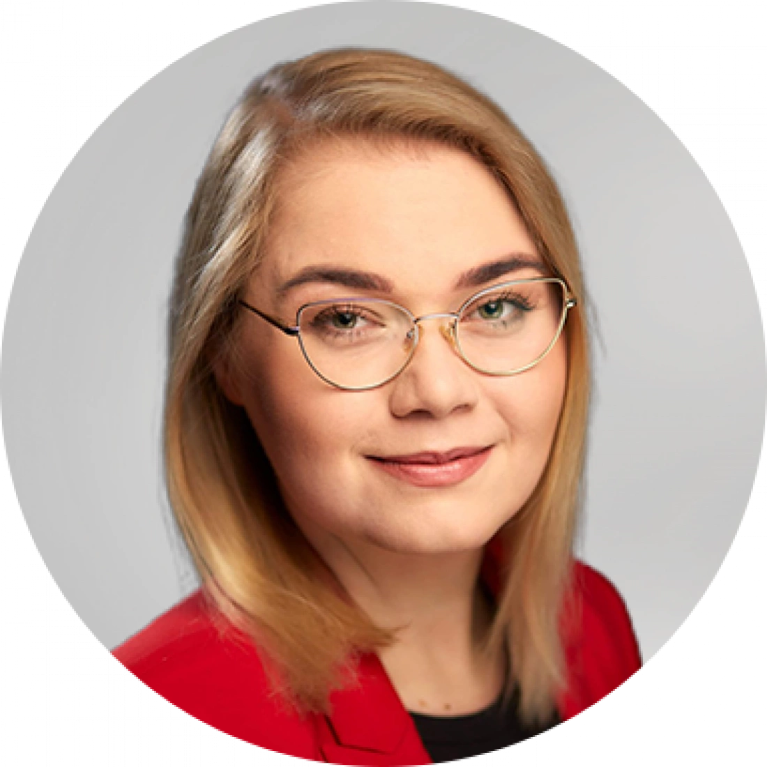 Młoda kobieta z krótkimi blond włosami, w okularach i czerwonym żakiecie, patrzy z uśmiechem.
