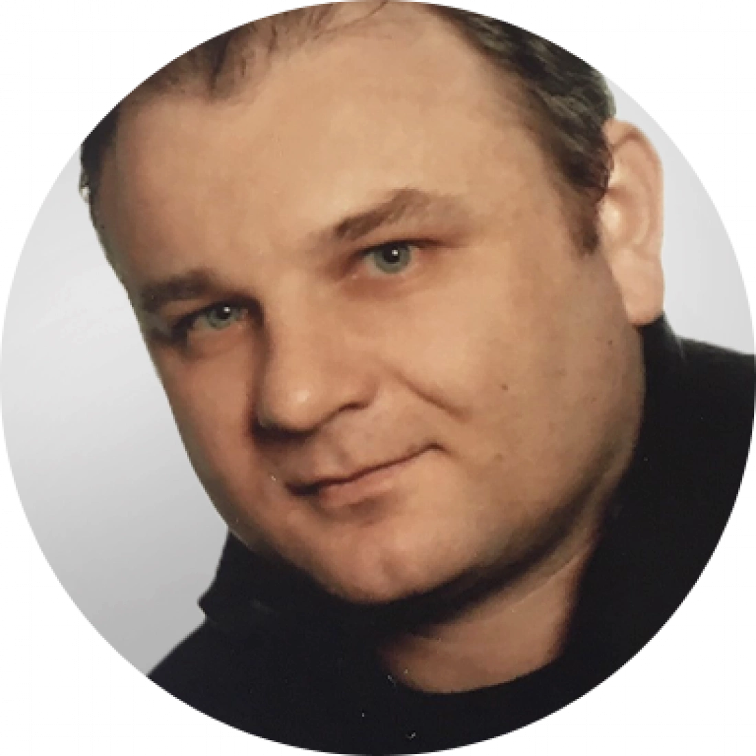 Mężczyzna z krótkimi włosami, uśmiechający się, na jasnym tle.