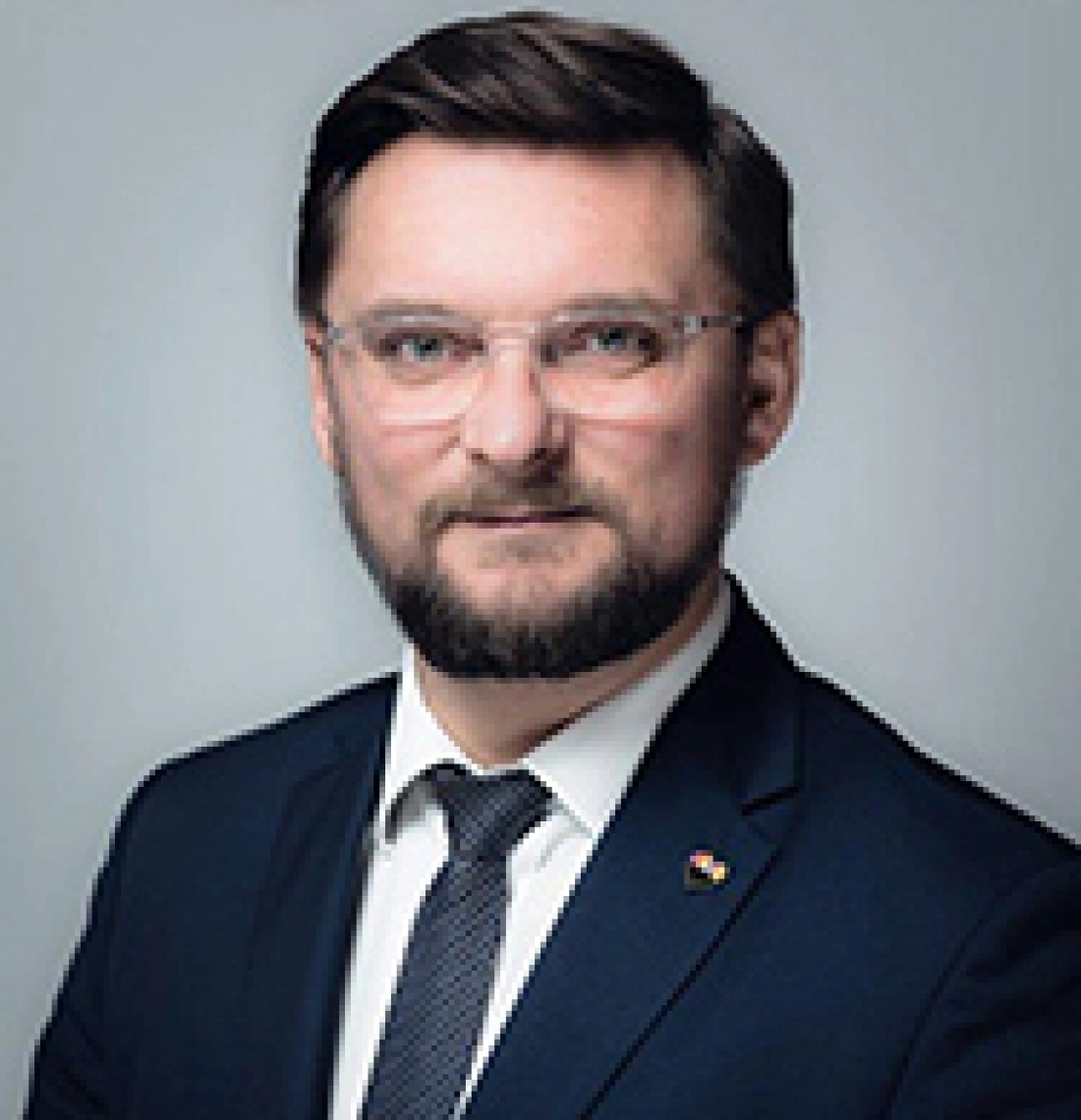 Mężczyzna w garniturze z okularami, uśmiechający się do kamery.