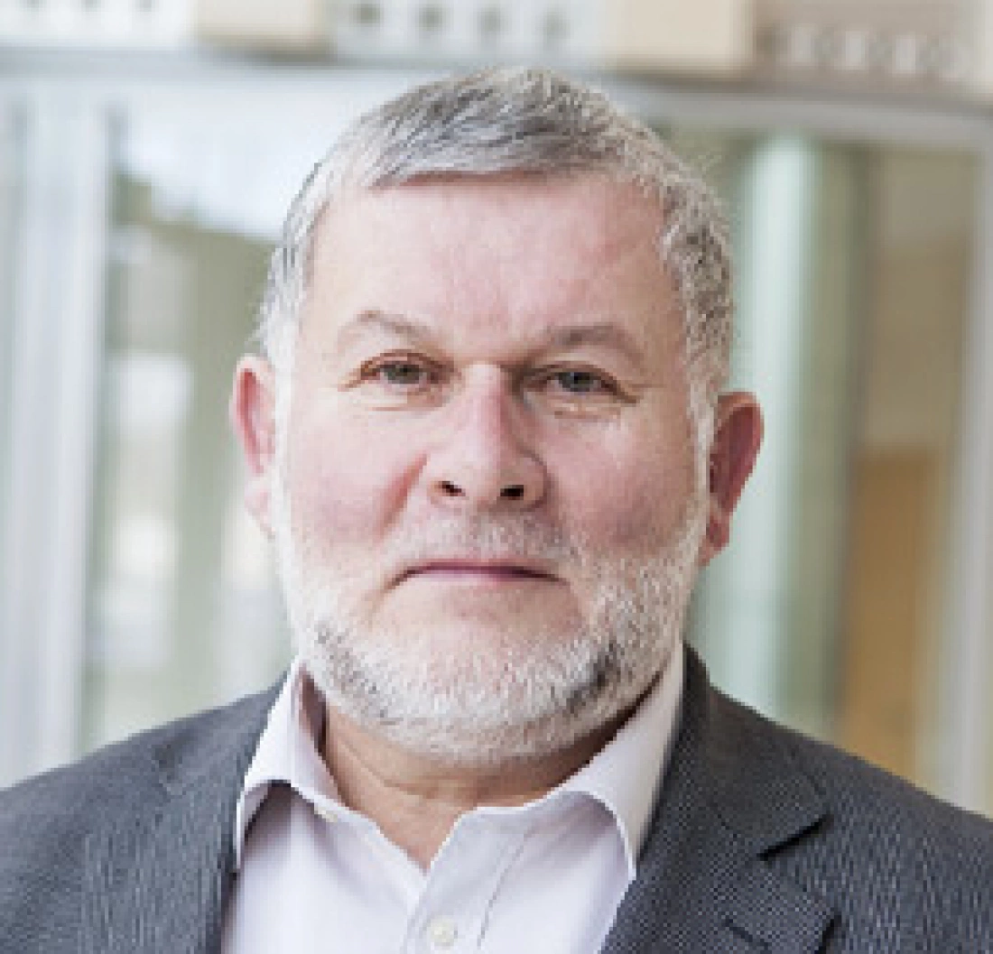 Mężczyzna z siwą brodą w garniturze, patrzący w stronę obiektywu.