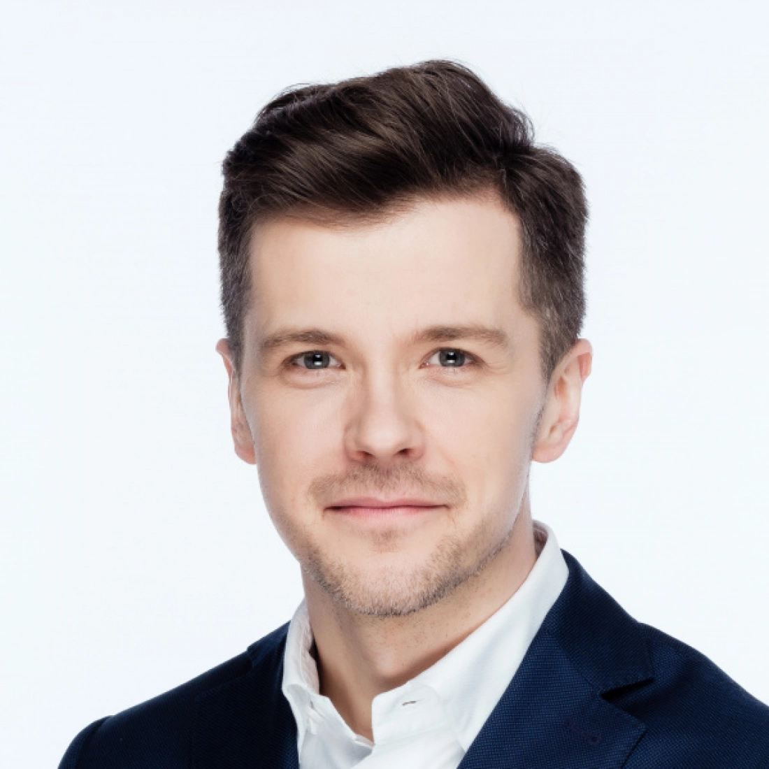 Mężczyzna w garniturze, uśmiechający się do kamery, na jasnym tle.