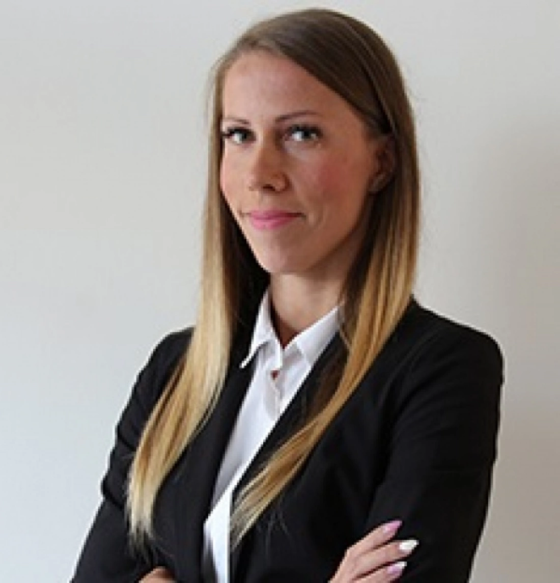 Kobieta w eleganckim garniturze stojąca z założonymi rękami na tle neutralnej ściany.