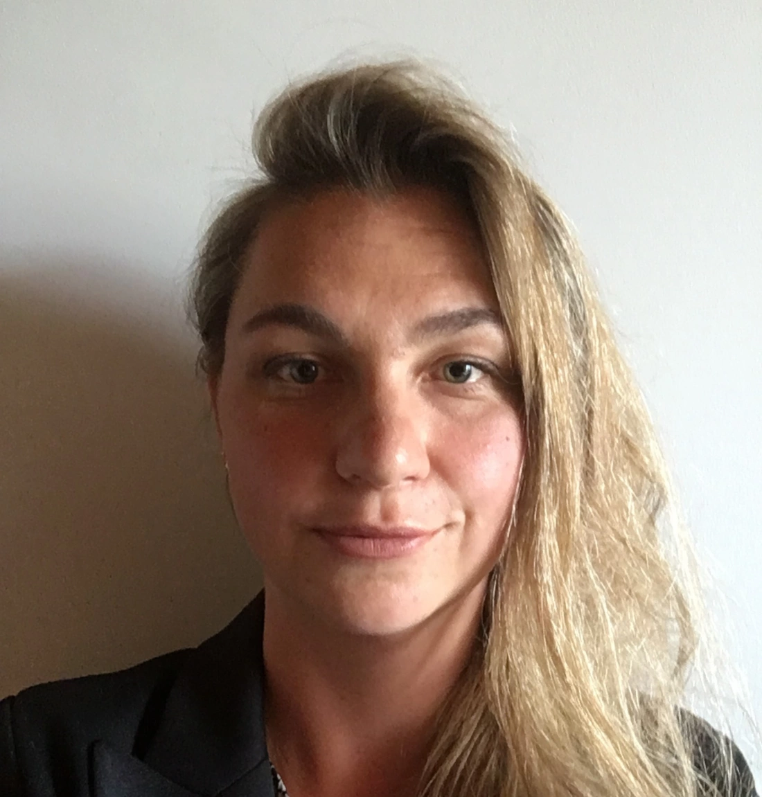 Portret osoby z długimi, falującymi włosami, uśmiechającej się na neutralnym tle.