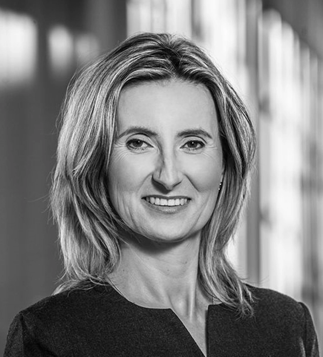 Kobieta z jasnymi włosami uśmiecha się w profesjonalnym otoczeniu.