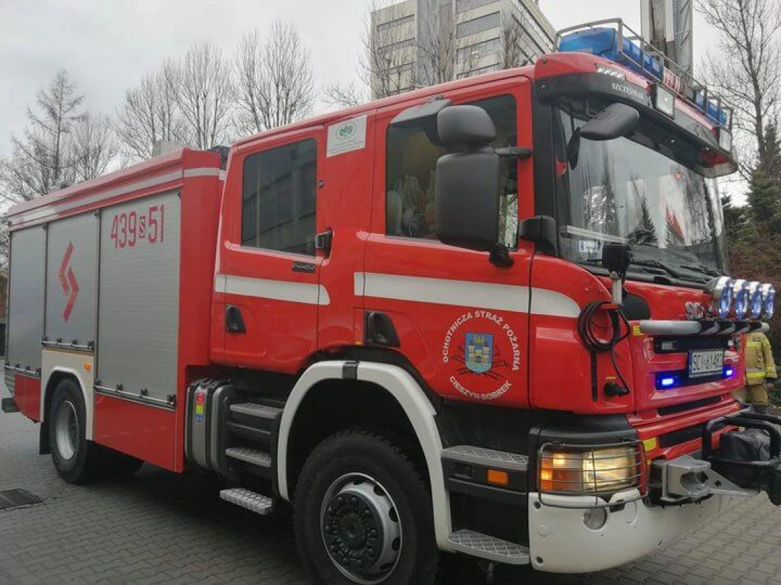 Czerwony wóz strażacki z oświetleniem, stojący na ulicy.