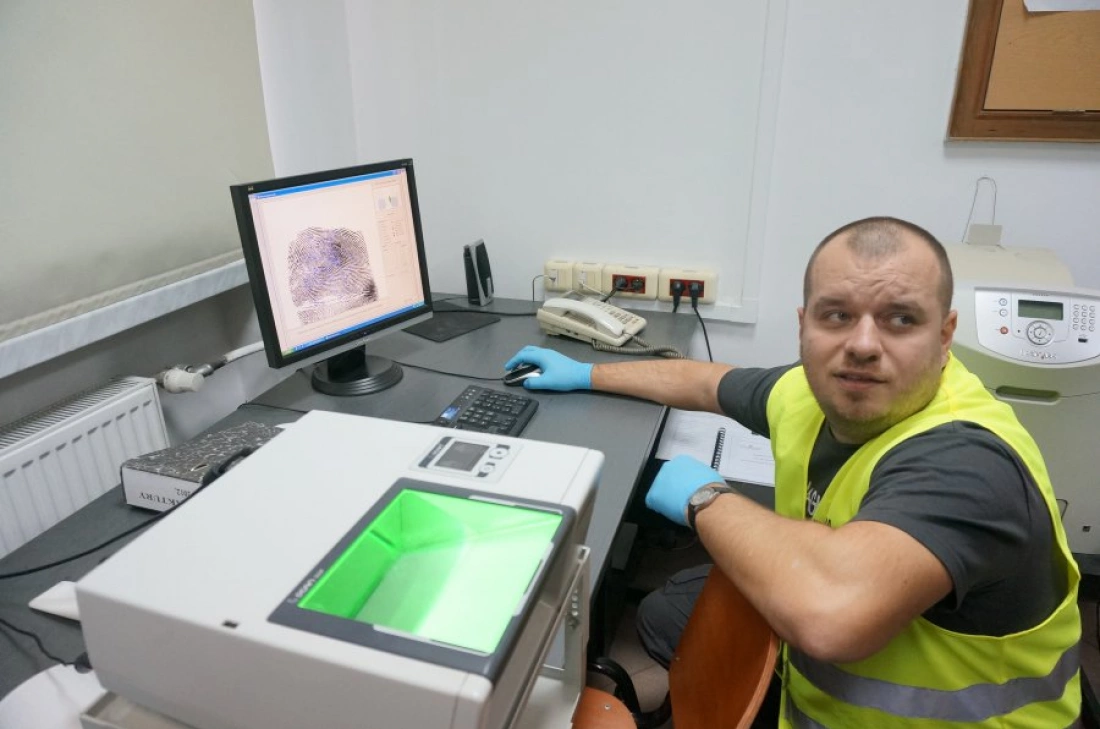 Mężczyzna w żółtej kamizelce siedzi przy biurku z komputerem, analizując dane na monitorze.