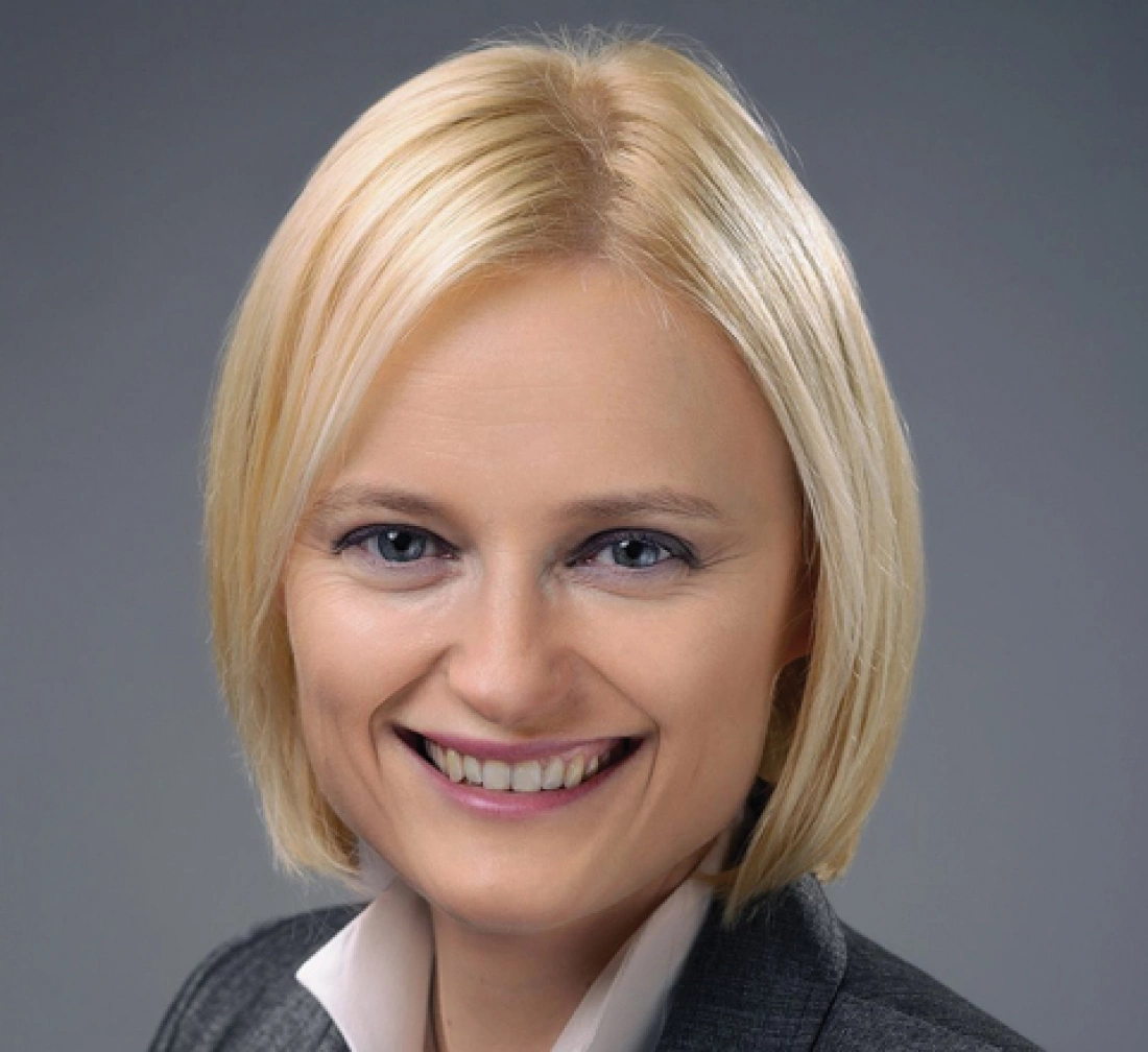 Portret uśmiechającej się kobiety z kr&oacute;tkimi blond włosami w garniturze.