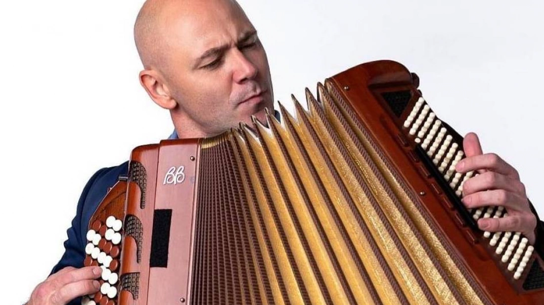 Mężczyzna gra na akordeonie, skupiony na wykonywanej muzyce.