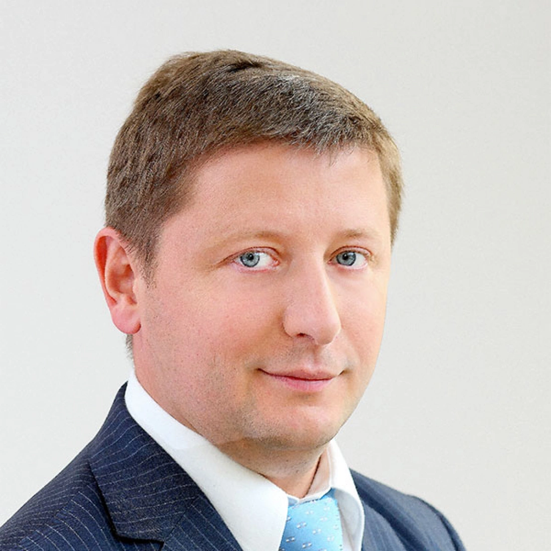 Mężczyzna w eleganckim garniturze z błękitnym krawatem, na jasnym tle.