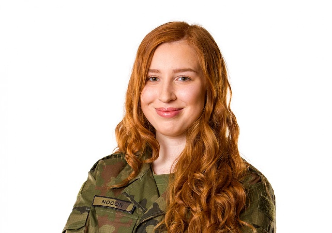 Młoda kobieta w mundurze wojskowym, uśmiechająca się do aparatu.