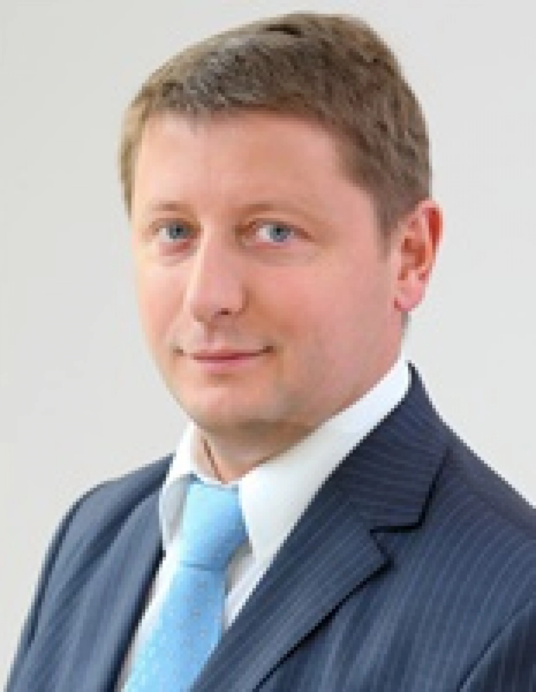 Mężczyzna w garniturze z niebieskim krawatem na neutralnym tle.