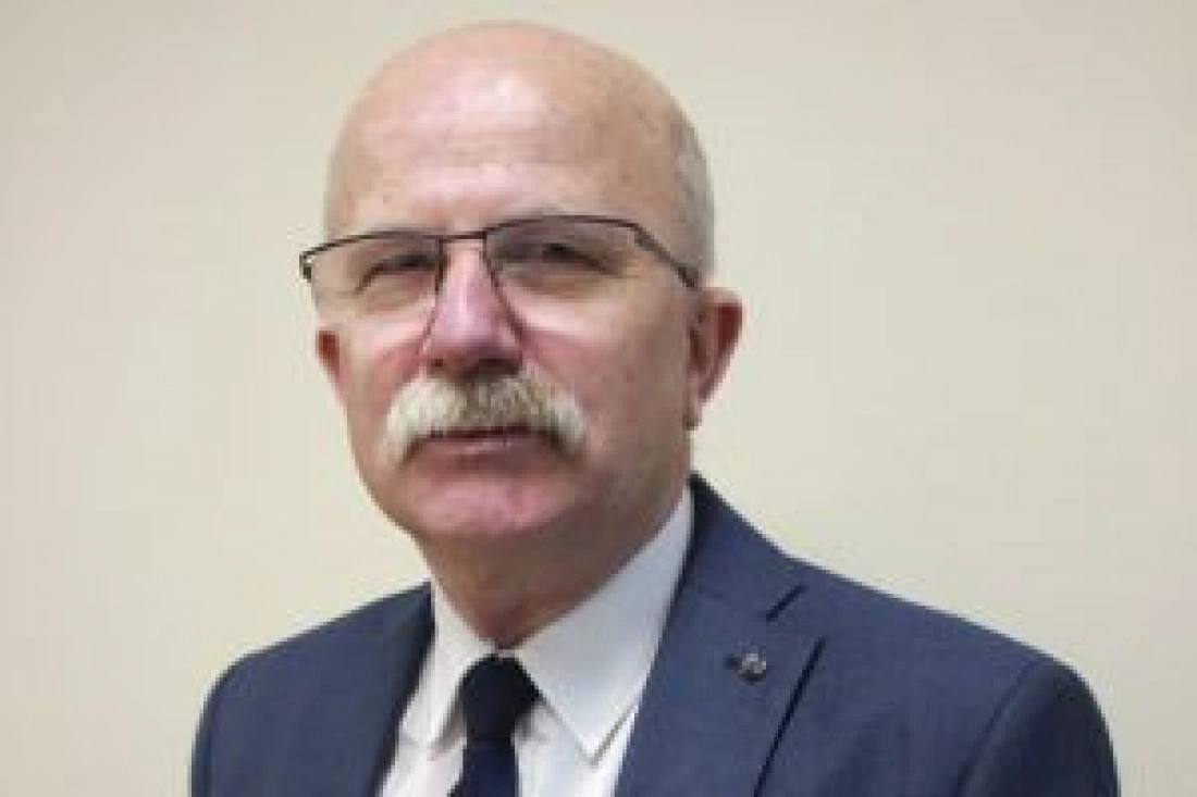 Mężczyzna w okularach, z wąsami, ubrany w elegancki garnitur.