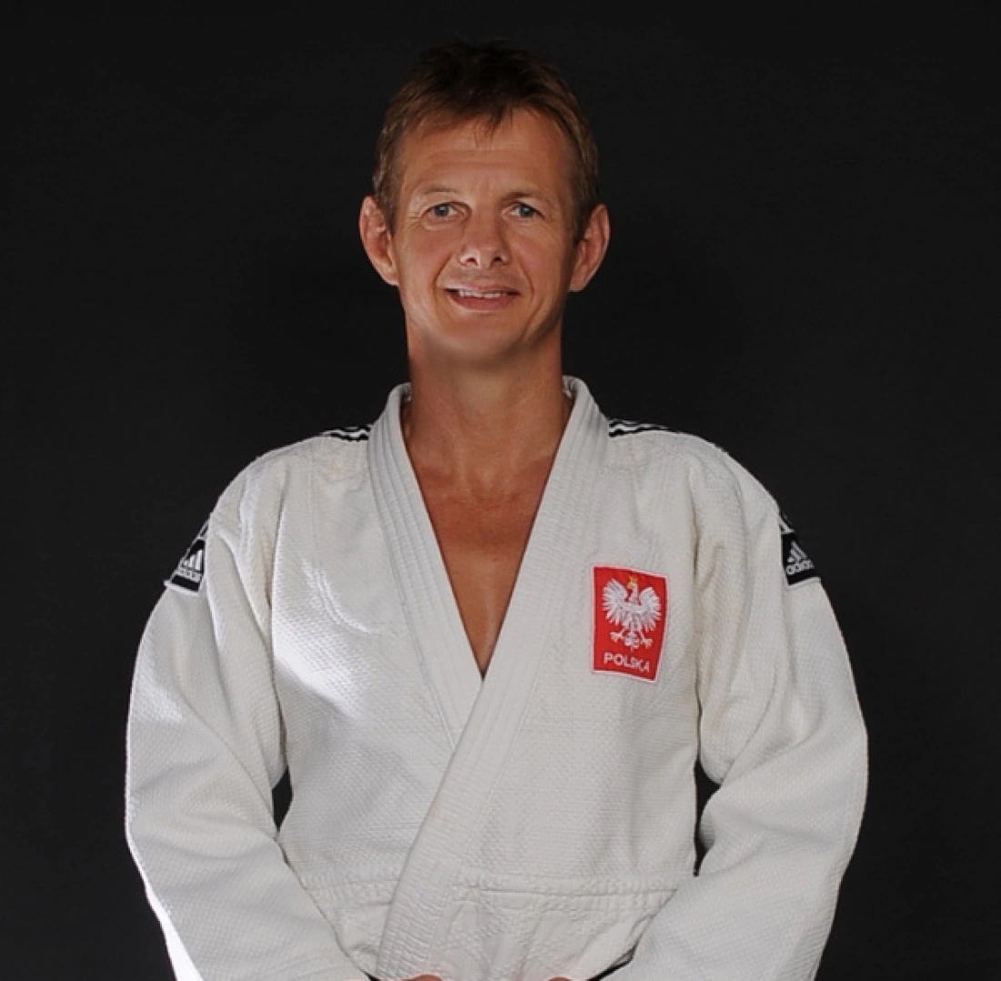 Mężczyzna w judodogu na czarnym tle, uśmiechający się.