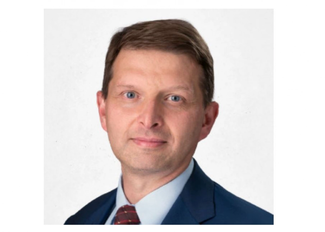 Mężczyzna w niebieskim garniturze z krawatem, o krótkich włosach i jasnych oczach, patrzy w kamerę.