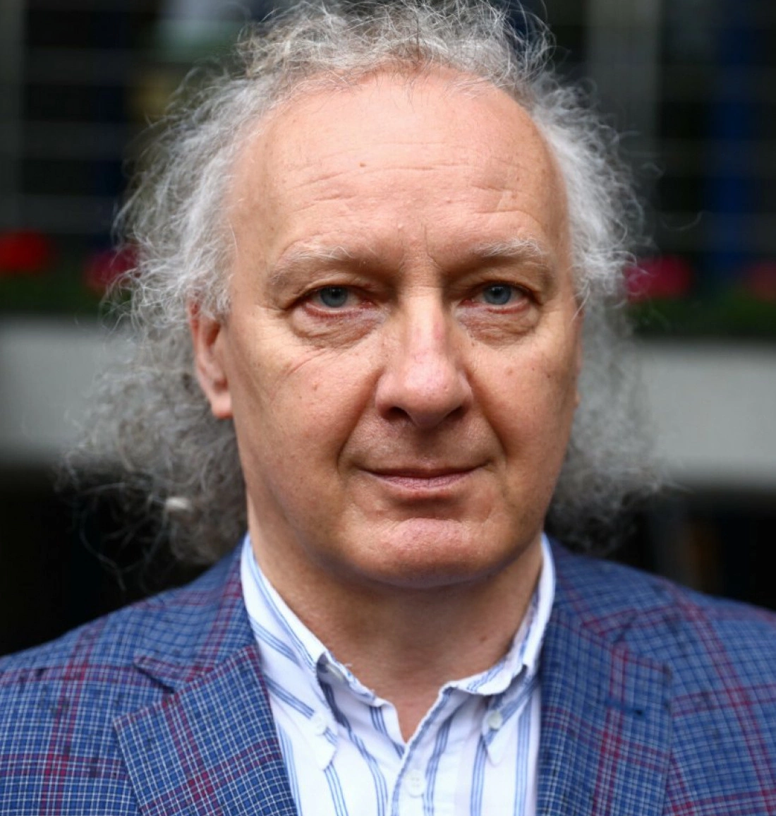 Mężczyzna o długich, kręconych włosach w niebieskiej koszuli i marynarce w kratę.