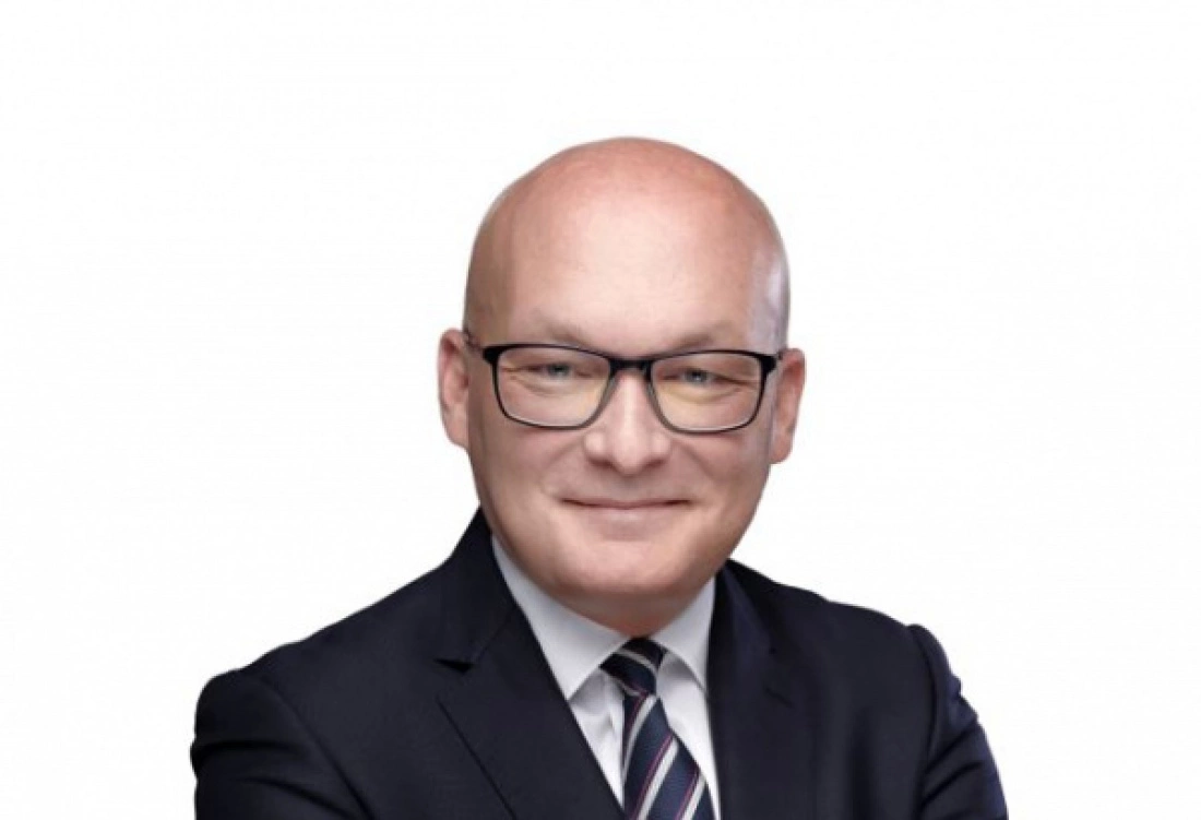 Mężczyzna w garniturze z okularami, uśmiechający się.